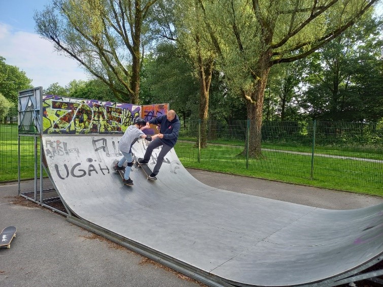 Ein Mann und ein Jugendlicher mit Skateboards in einer Halfpipe