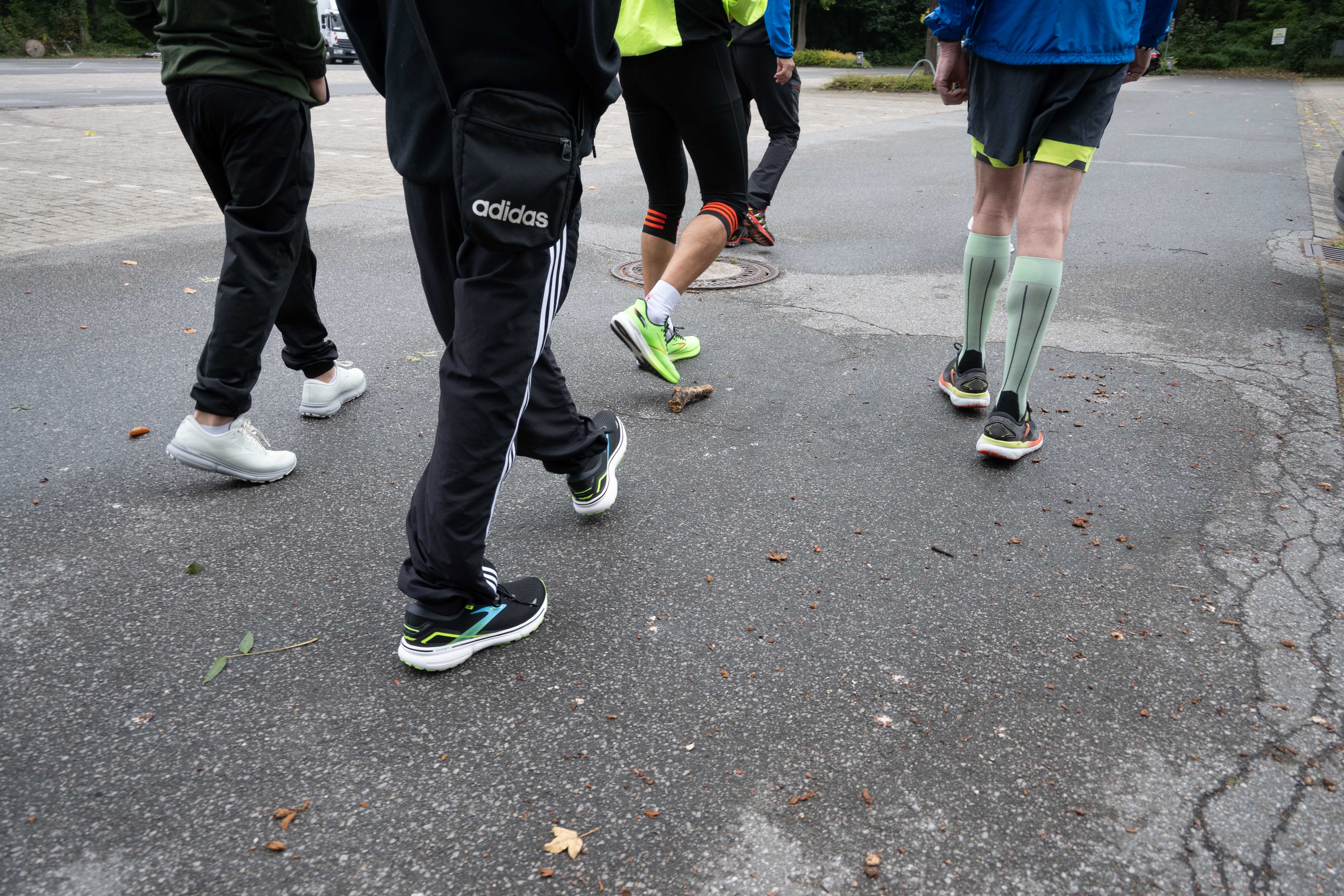 Fünf Personen in Sportkleidung gehen auf einem Asphaltweg. Es werden nur ihre Beine gezeigt.